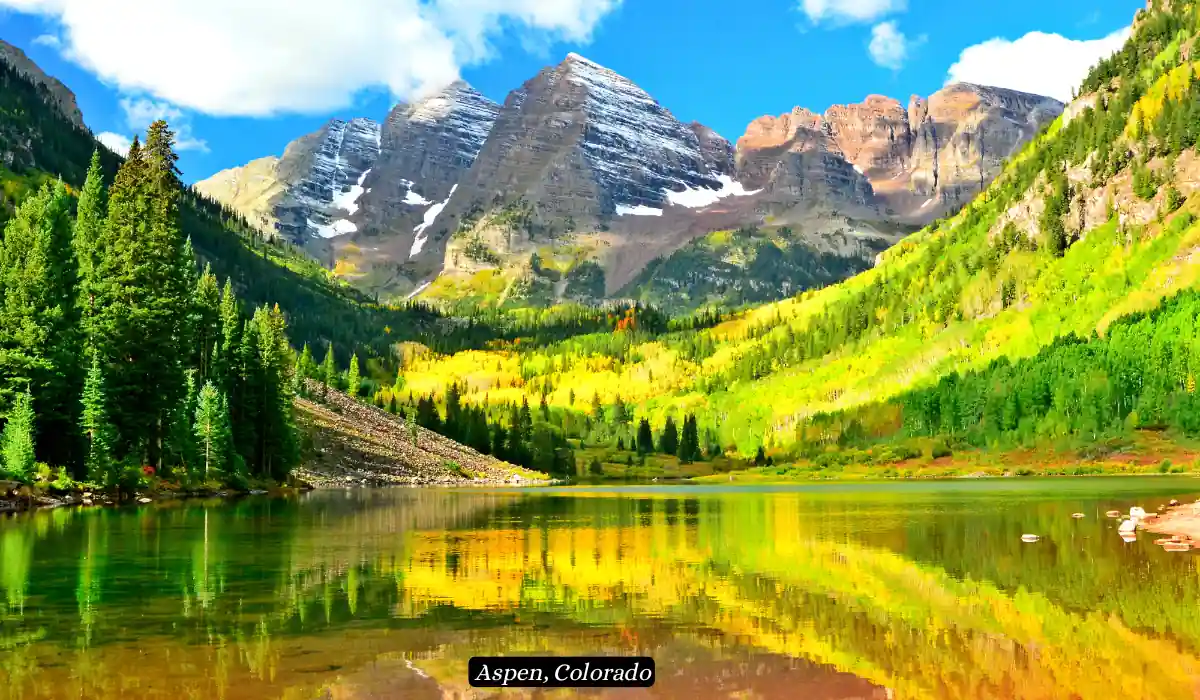 12 Best Places to Visit in November for Couples 2025 15 A serene mountain landscape in Aspen, Colorado, showcasing the Maroon Bells. The snow-capped peaks tower over vibrant green forests and a reflective, tranquil lake, capturing the beauty of nature under a bright blue sky.