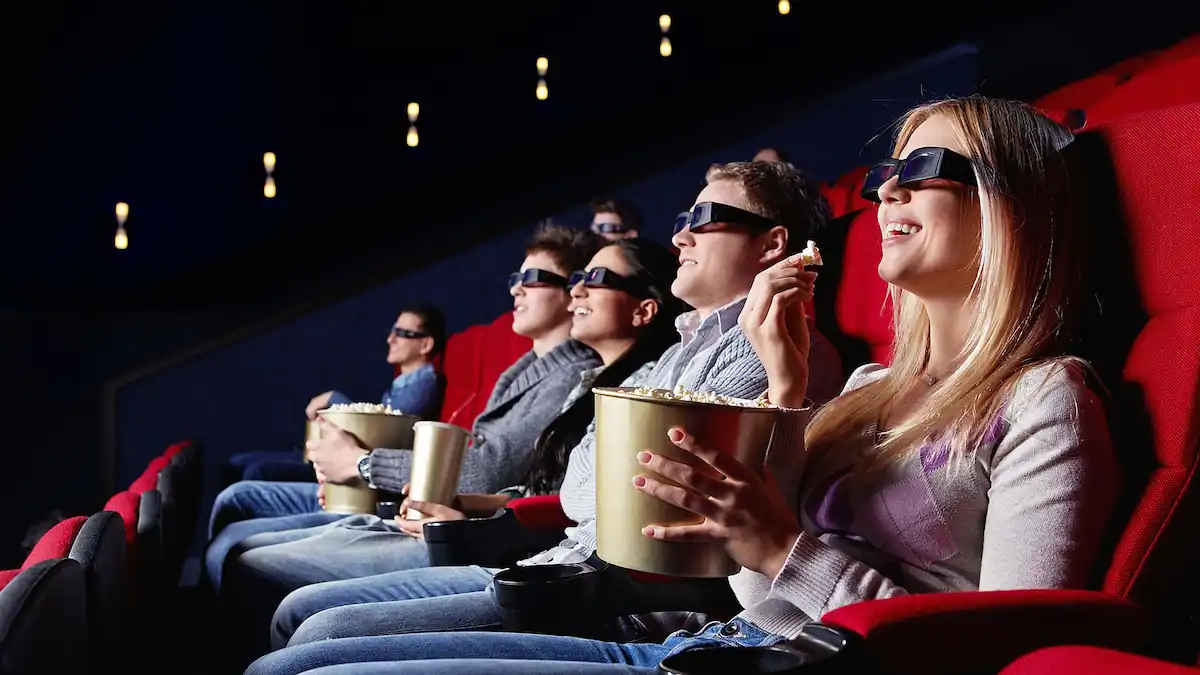 15 Romantic Things To Do in New Haven For Couples in 2024 13 A group of people in a movie theater sits in red seats, wearing 3D glasses and holding buckets of popcorn. They appear engaged and entertained by what they are watching on the screen. The theater is dark, and their faces are illuminated by the screen's light.