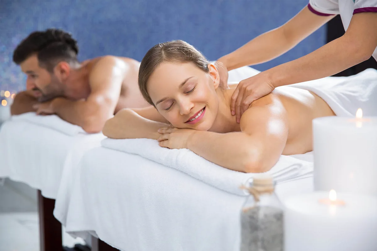 15 Romantic Things To Do in New Haven For Couples in 2024 11 A man and a woman are lying on massage tables receiving massages. The woman is smiling with her eyes closed while a massage therapist works on her back. The man, also with his eyes closed, is getting a back massage in the background. Candles are visible in the foreground.