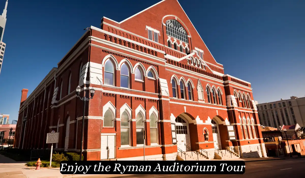 Top 15 Romantic Things to do in Nashville Tennessee for Couples 5 A red brick Gothic Revival building with arched windows and a peaked roof stands prominently under a clear blue sky. The text "Enjoy the Ryman Auditorium Tour" is at the bottom of the image.