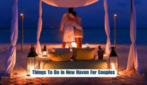 A couple stands embraced under a canopy on a beach at night, surrounded by lit lanterns. There is a cozy setting with cushions and a table. The scene is romantic and serene. Text at the bottom reads, "Things To Do in New Haven For Couples.