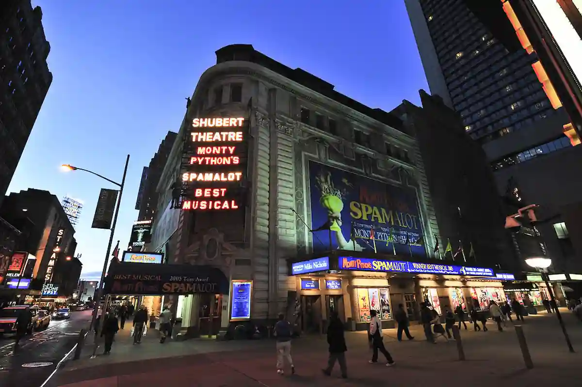15 Romantic Things To Do in New Haven For Couples in 2024 8 A street view at dusk showcases the Shubert Theatre in the city. The marquee advertises "Monty Python's Spamalot," highlighted as the "Best Musical." Pedestrians pass by the brightly lit entrance, and the building’s historic architecture stands out against the twilight sky.