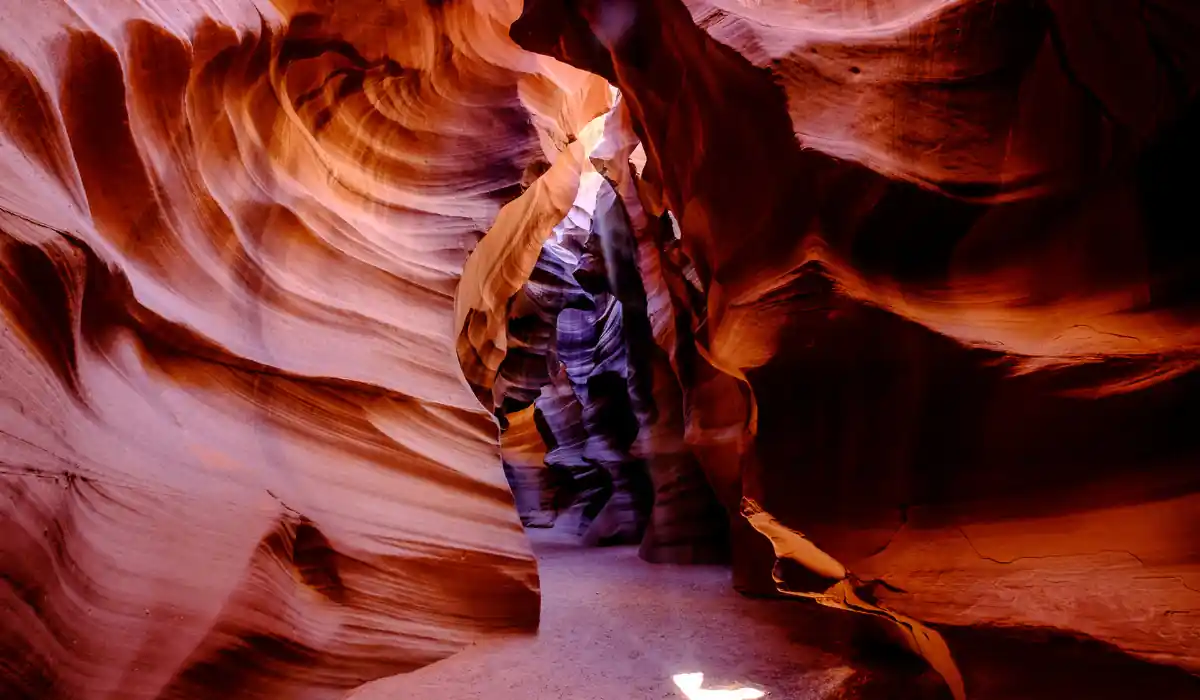 Top 15 Fun $ Unique Places That Don't Feel Real in the USA 2025 13 A stunning view of Antelope Canyon with smooth, swirling sandstone walls in warm shades of orange and red. A narrow path winds through the canyon, with a bright beam of light illuminating the ground.