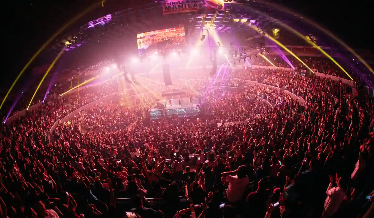 20 Most Romantic Things to do in California for Couples 18 A vibrant, packed arena filled with cheering spectators and colorful stage lights. The central ring is illuminated under a canopy of beams and spotlights, creating a lively and energetic atmosphere. A large screen hangs overhead displaying the event.