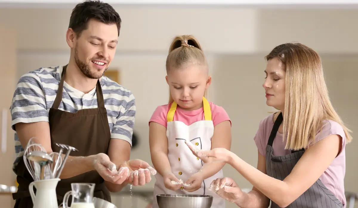 40 amazing Cute Date Ideas in Columbus, Ohio for Couples in 2025 30 A family of three, wearing aprons, stand around a kitchen counter. The father and daughter are mixing ingredients in a bowl, while the mother looks on, guiding them. They are smiling and engaged in the cooking activity together.