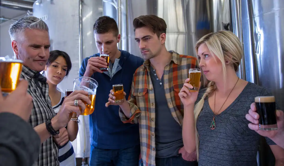 40 amazing Cute Date Ideas in Columbus, Ohio for Couples in 2025 24 A group of people stand together in a brewery, each holding a glass of beer. They appear to be sampling and examining the beverages, with large metal tanks in the background. The atmosphere is focused and curious.