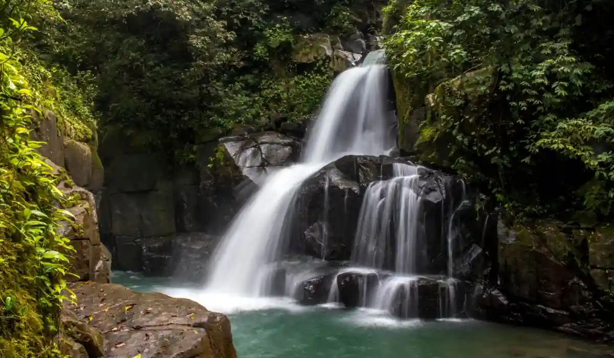 Top 15+ Free Things to do in Atlanta for Couples 2025 10 A serene waterfall cascades over smooth, dark rocks into a turquoise pool, surrounded by lush green foliage. Sunlight filters through the dense canopy, creating a peaceful, natural scene.