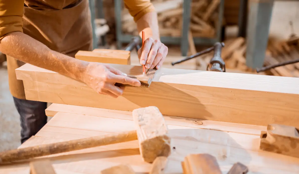 40 amazing Cute Date Ideas in Columbus, Ohio for Couples in 2025 16 A person wearing an apron uses a square ruler and pencil to mark measurements on a wooden plank in a workshop. Various carpentry tools, such as a hammer and wood pieces, are on the workbench.