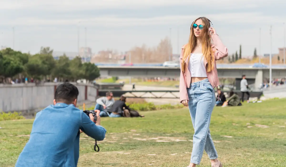 40 amazing Cute Date Ideas in Columbus, Ohio for Couples in 2025 35 A woman poses outdoors in casual attire, wearing sunglasses and a pink jacket, as a photographer in a blue jacket takes her picture. They are in a park with grass and trees, and a bridge in the background.