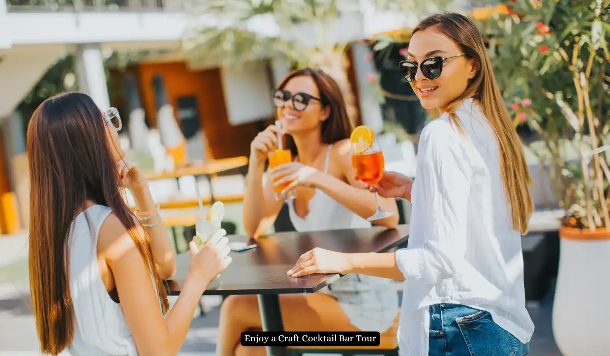 Top 15+ Romantic Things to do in Portland for Couples 11 Three women are enjoying drinks at an outdoor table, wearing sunglasses and casual summer attire. They are smiling and engaged in conversation, with plants and a building in the background.