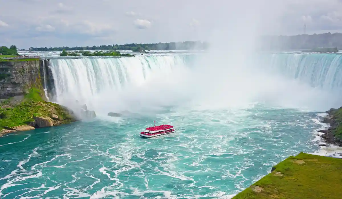 Top 12+ Romantic Things to Do in Buffalo for Couples in November 9 A vibrant red tour boat sails near the powerful Horseshoe Falls at Niagara Falls, surrounded by mist and churning waters. Lush green cliffs and a cloudy sky form the backdrop, highlighting the majestic beauty of the cascading waterfall.