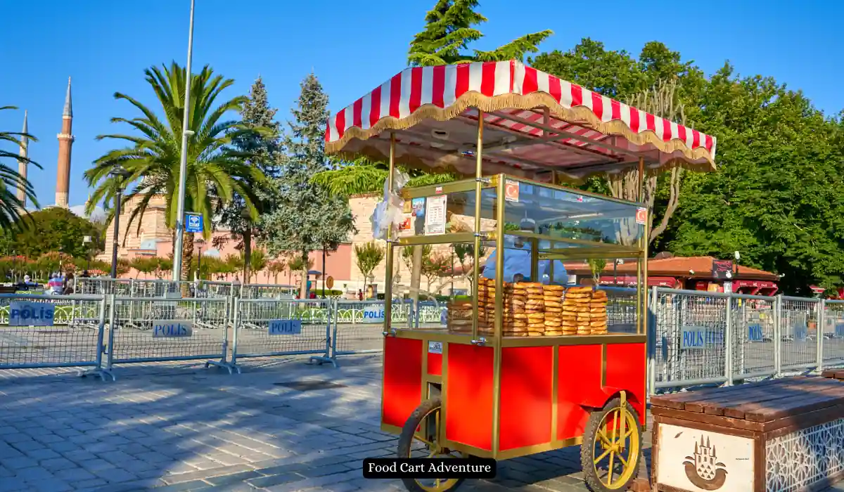 Top 15+ Romantic Things to do in Portland for Couples 18 A red and yellow food cart with striped canopy sells simit on a sunny day. The cart is on a paved path with trees and a historic building's dome and minaret in the background. A sign reads "Food Cart Adventure.