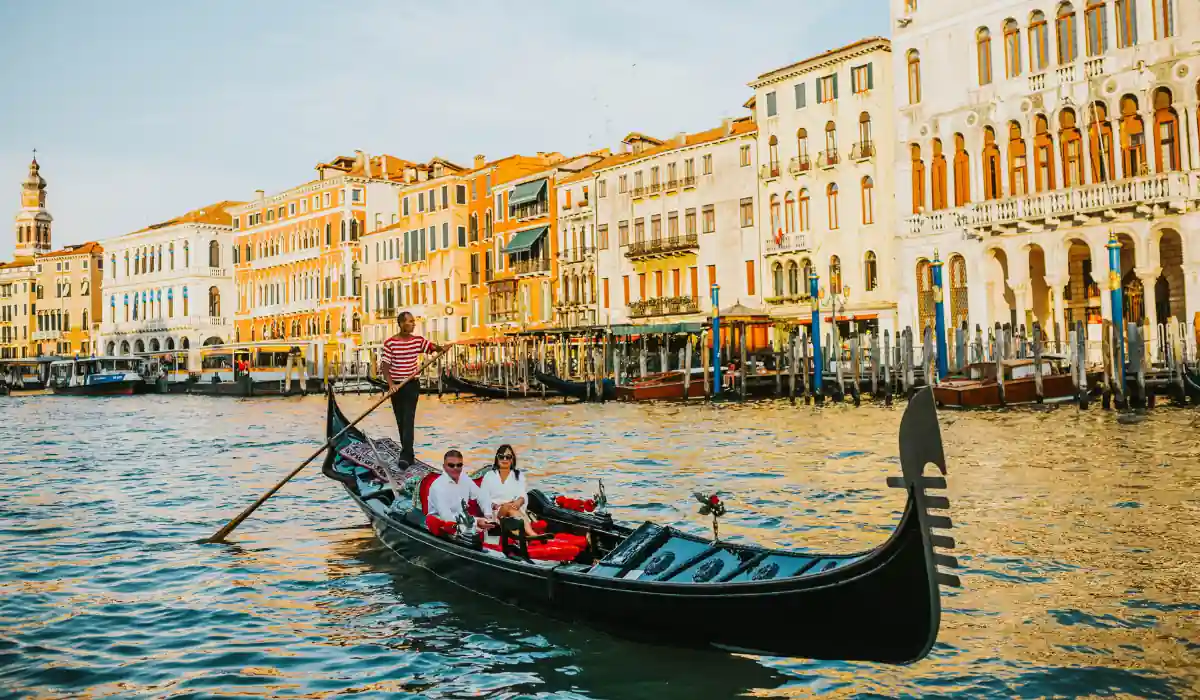 20 Most Romantic Things to do in California for Couples 22 A gondolier navigates a traditional gondola carrying two passengers along a sunlit canal in Venice. Historic buildings with colorful facades line the waters edge under a clear blue sky.