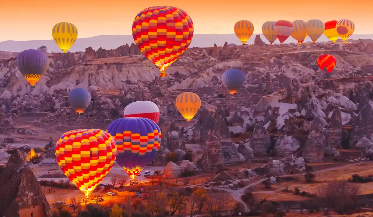 20 Most Romantic Things to do in California for Couples 5 Hot air balloons of various colors rise over the rocky landscape of Cappadocia at sunrise. The sky is a gradient of orange hues, and the unique rock formations are visible on the ground.