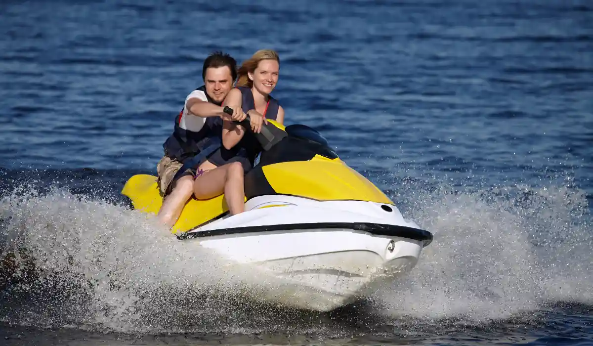 12+ Best Things to do in San Diego for Couples 2025 16 A smiling couple rides a yellow and white jet ski across blue water, creating splashes as they move. The man is in front steering, while the woman holds on behind him. Both are wearing life jackets.
