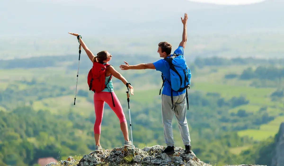 40 amazing Cute Date Ideas in Columbus, Ohio for Couples in 2025 38 Two hikers with backpacks stand on a rocky cliff, arms raised in celebration. They overlook a vast, green landscape with rolling hills, enjoying a scenic view. Both hold hiking poles and appear joyful, embracing the adventure.