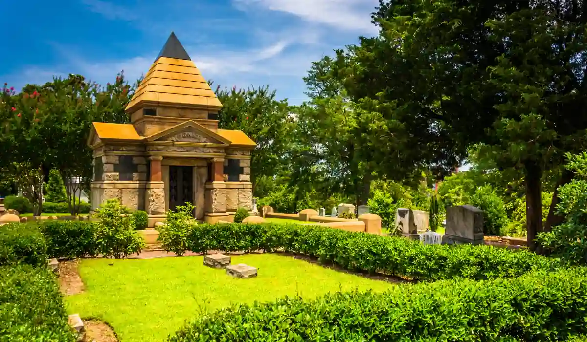 Top 15+ Free Things to do in Atlanta for Couples 2025 5 A historic cemetery with a small, ornate stone mausoleum featuring a triangular roof. It is surrounded by tombstones and lush greenery, under a bright blue sky with scattered clouds.