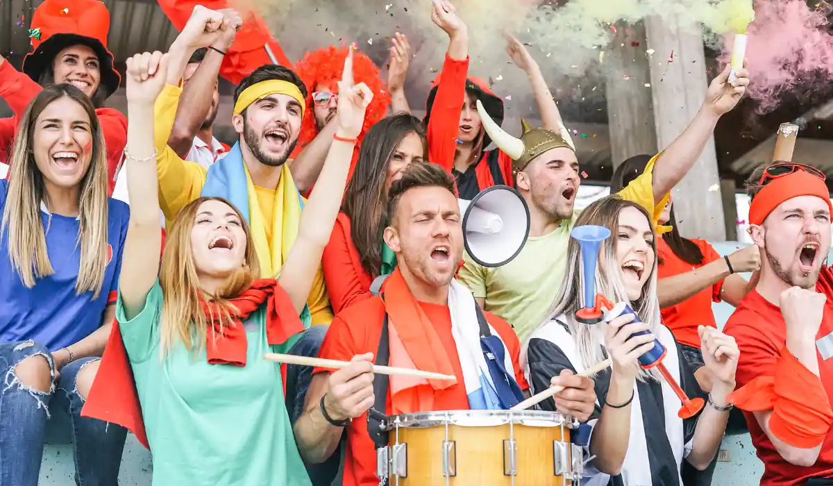 40 amazing Cute Date Ideas in Columbus, Ohio for Couples in 2025 40 Enthusiastic sports fans cheer in a stadium, wearing colorful clothes and holding a megaphone and drum. Some have painted faces, and colorful smoke fills the air as they express excitement and support for their team.