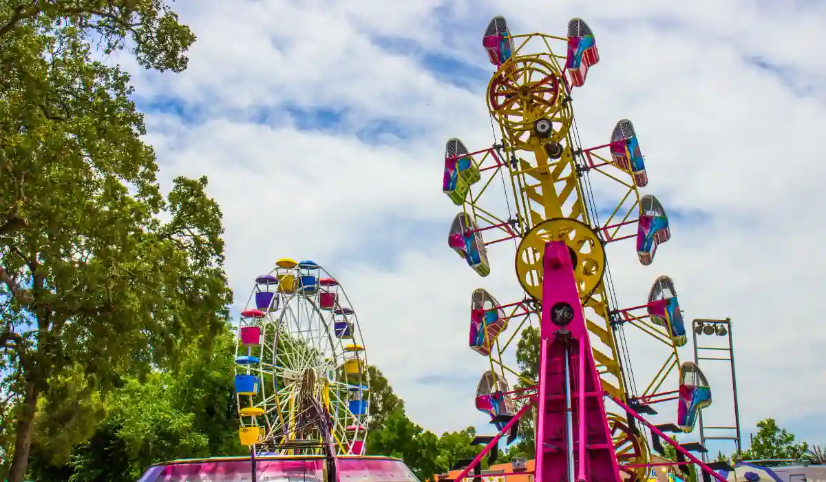 40 amazing Cute Date Ideas in Columbus, Ohio for Couples in 2025 36 A vibrant amusement park scene featuring a colorful Ferris wheel and a towering thrill ride, surrounded by lush green trees under a partly cloudy blue sky.
