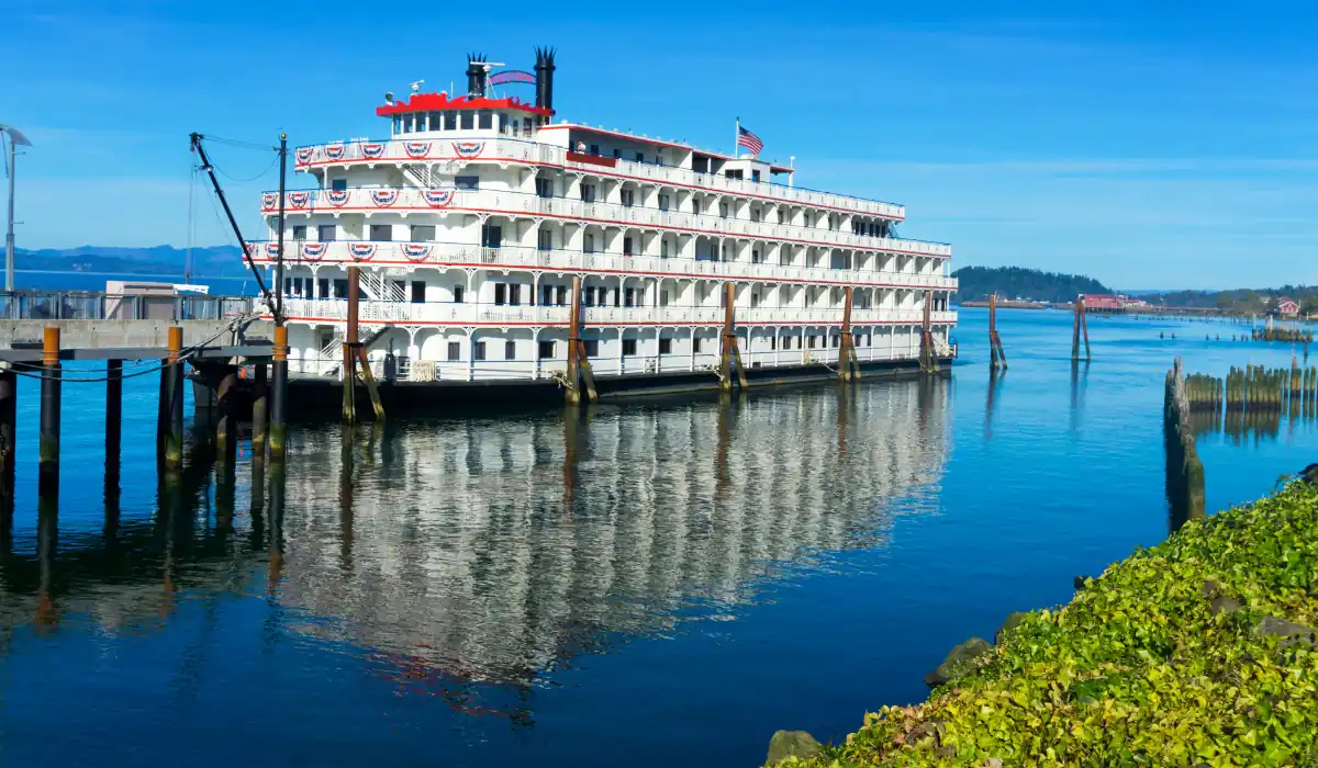 40 amazing Cute Date Ideas in Columbus, Ohio for Couples in 2025 39 A large, multi-deck paddle steamer with an American flag is moored at a dock on a calm river. The blue sky and distant hills are reflected in the water. Green foliage lines the foreground.