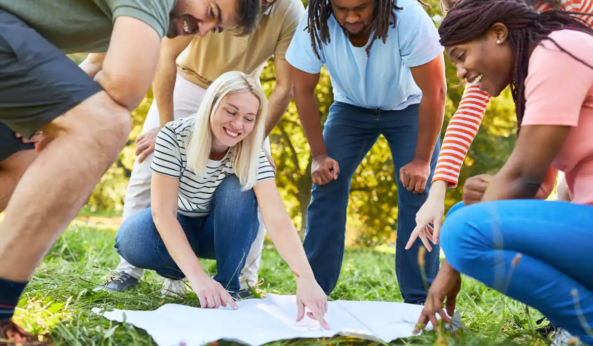 40 amazing Cute Date Ideas in Columbus, Ohio for Couples in 2025 7 A group of people outdoors, bent over a large white sheet on the grass. They are smiling and pointing at the sheet, appearing engaged and happy. Sunlight filters through the trees, creating a lively and bright atmosphere.