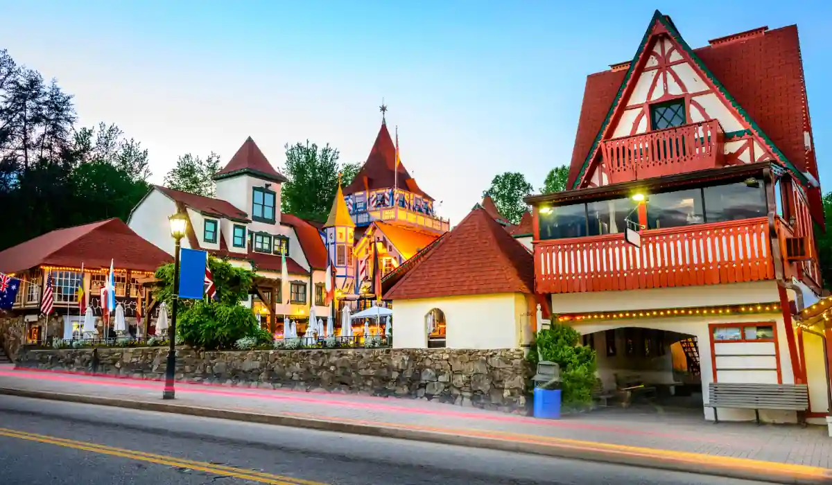 Top 15 Fun $ Unique Places That Don't Feel Real in the USA 2025 10 A picturesque view of Helen, Georgia, showcasing Bavarian-style architecture with colorful timber-frame buildings. The street features blurred lights from passing cars, and theres lush greenery in the background under a twilight sky.