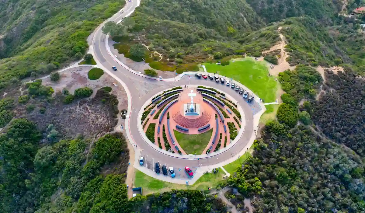 12+ Best Things to do in San Diego for Couples 2025 12 Aerial view of a circular amphitheater surrounded by greenery and a winding road. Cars are parked around the circular structure. The landscape features hilly terrain with dense vegetation.
