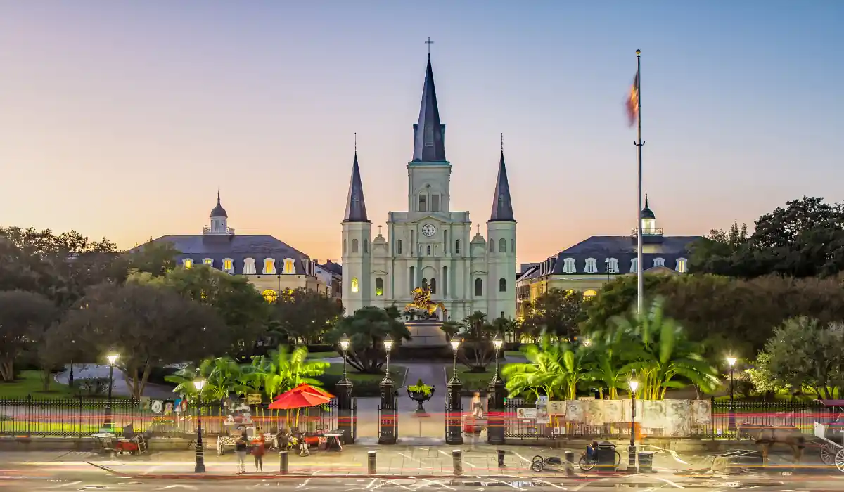 The 15 Best Things to Do in New Orleans for Couples 3 St. Louis Cathedral at dusk in New Orleans, with its iconic spires, stands dramatically against the evening sky. In the foreground, a lively Jackson Square features a statue, people, street vendors, and light trails from passing vehicles.