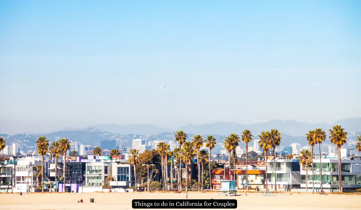 20 Most Romantic Things to do in California for Couples 2 A sunny beach scene in California with palm trees, colorful beachfront houses, and distant mountains. The sky is clear and bright, offering a picturesque coastal view. A banner on the image reads, Things to do in California for Couples.