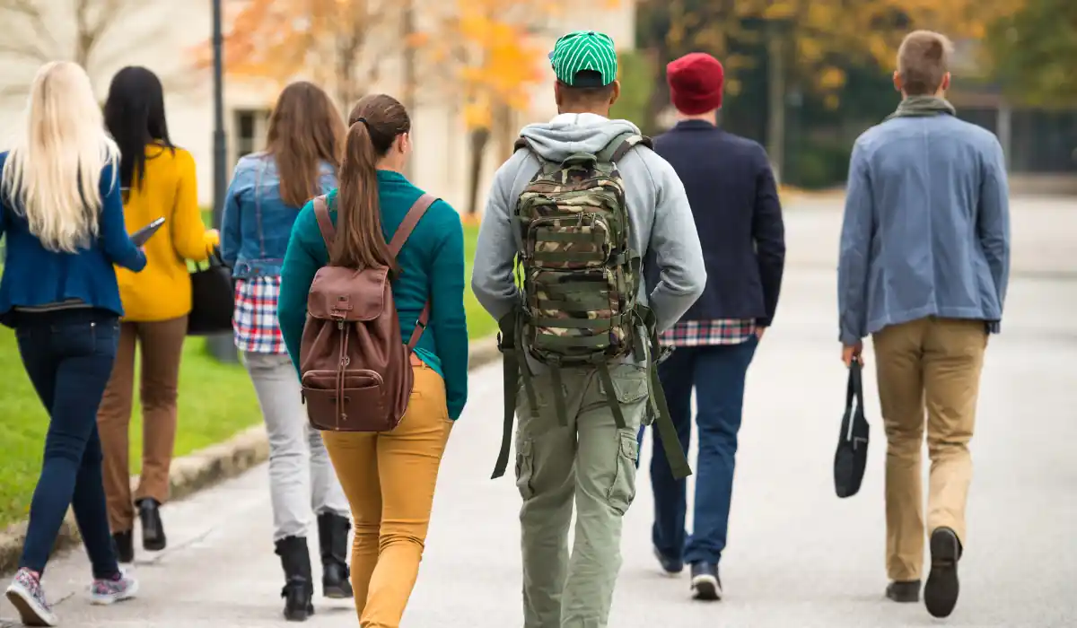The 15 Best Things to Do in New Orleans for Couples 8 A group of people walking away on a street, wearing casual fall clothing. Some have backpacks and a variety of hairstyles and colors. The background has trees with autumn leaves and a building visible.