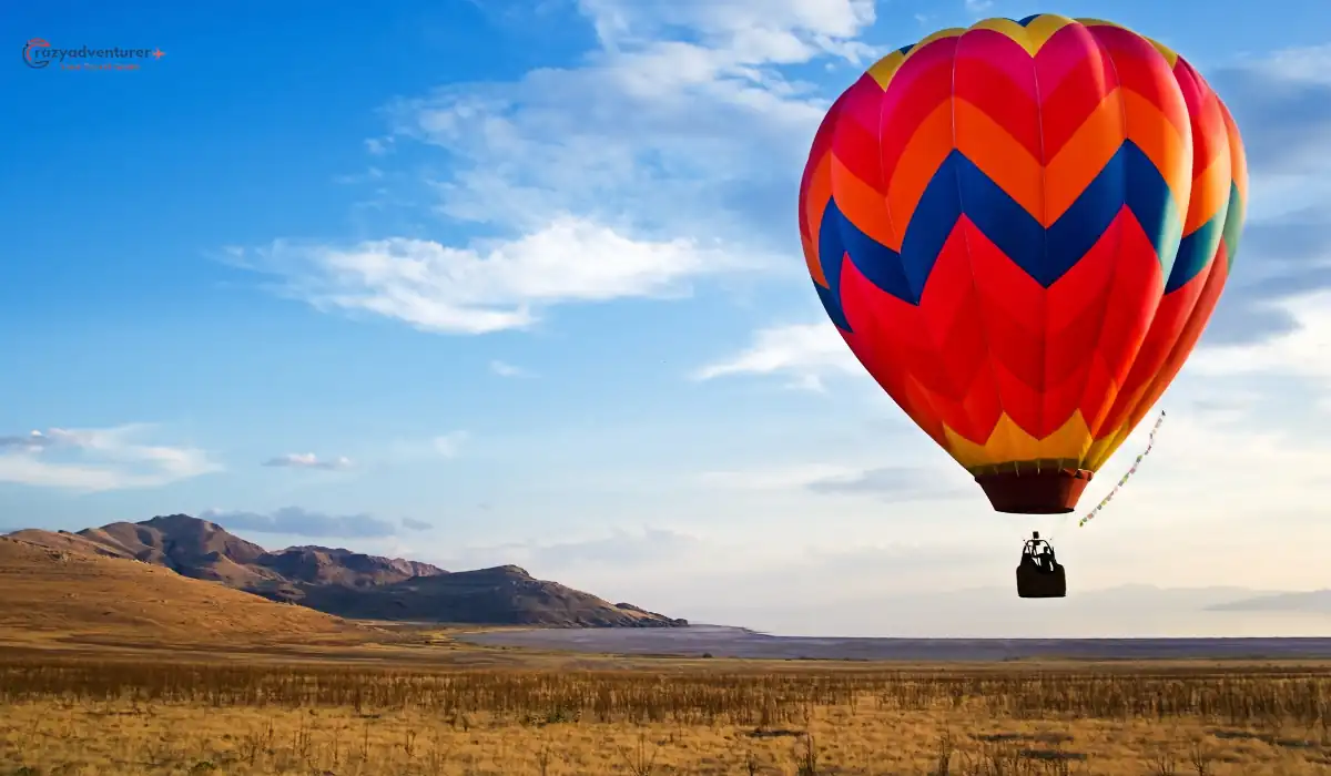 15+ Fun and Romantic Things To Do In Houston for Couples 13 A colorful hot air balloon with a vibrant zigzag pattern floats above a vast, open landscape with dry grass and distant hills under a clear blue sky.