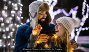 A couple in warm clothing is playfully wrapped in string lights, smiling at each other outdoors at night. The background features softly glowing white lights, creating a festive and romantic atmosphere. "Romantic Things to Do at Night for Couples"