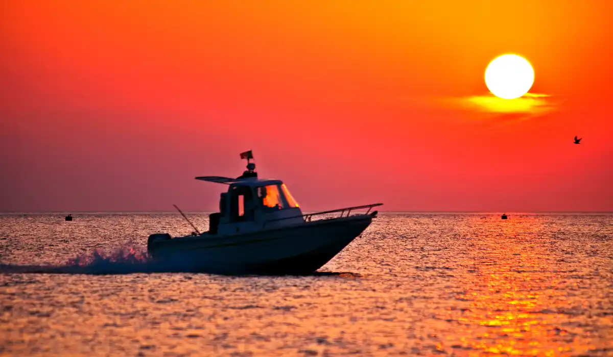 15+ Fun and Romantic Things To Do In Houston for Couples 11 A silhouette of a boat speeds across the water at sunset, with the sun setting in a vibrant orange and red sky. A small bird is flying to the right, and the ocean reflects the warm colors of the sky.
