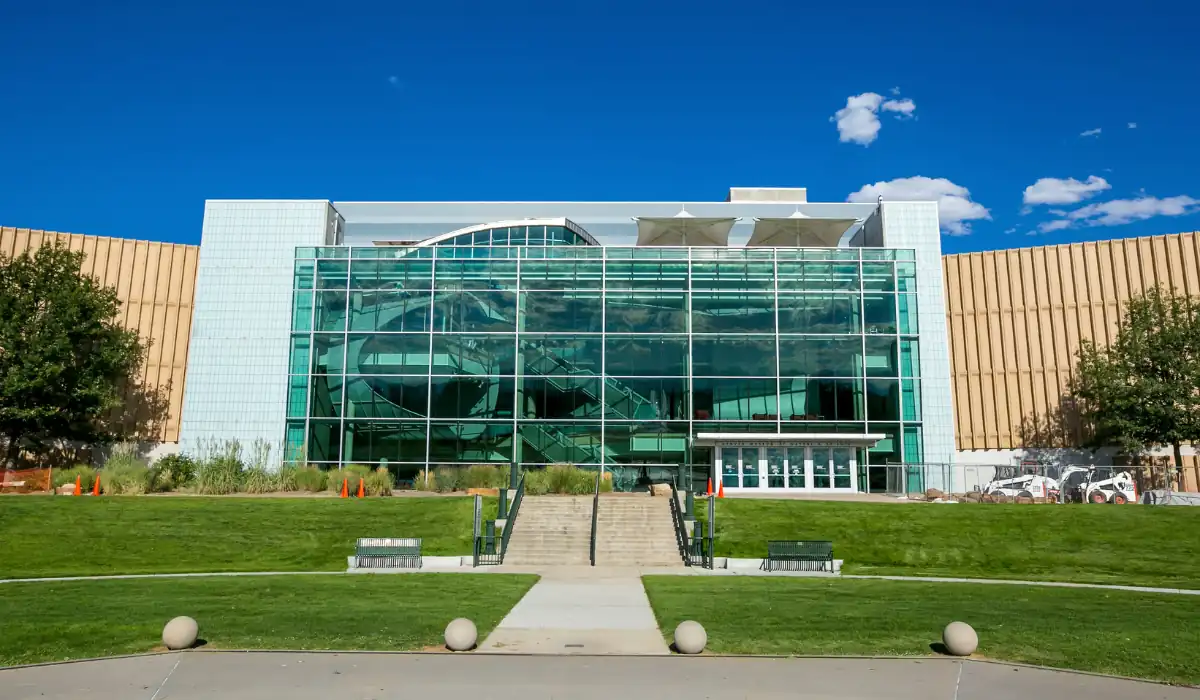 15+ Fun and Romantic Things To Do In Houston for Couples 4 A modern building with a large glass facade reflecting the blue sky and white clouds. It is surrounded by green lawns and trees, with steps leading to the entrance. The structure features a blend of glass and light-colored materials.