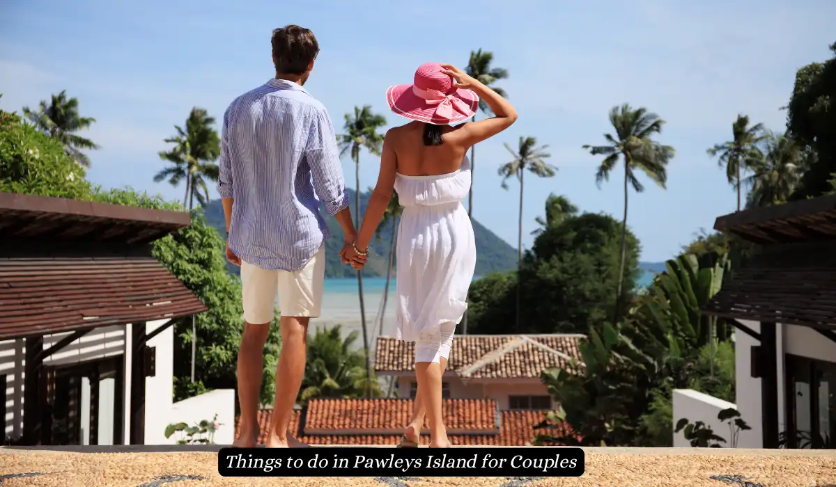 A couple holding hands, facing towards a tropical view with palm trees and the ocean. The woman wears a pink sunhat and white dress, while the man is in a light shirt and shorts. The text reads, Things to do in Pawleys Island for Couples.