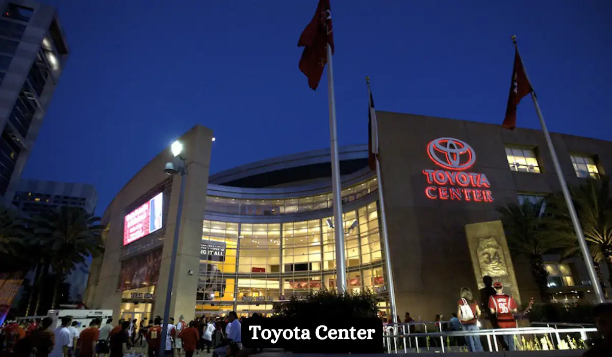 15+ Fun and Romantic Things To Do In Houston for Couples 14 Night view of Toyota Center with its brightly lit glass facade. American flags and people in sports jerseys are visible in the foreground.