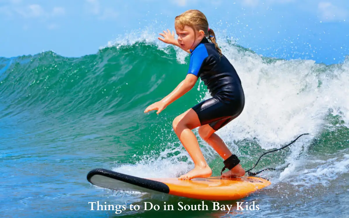 Top 15+ Fun Things to Do in South Bay Kids this Weekend 1 Young child surfing on a small wave, wearing a blue and black wetsuit. The ocean is vibrant blue with foamy waves. Text at the bottom reads, Things to Do in South Bay Kids.