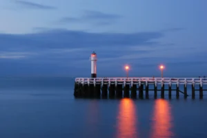 A tranquil scene of a lighthouse at the end of a pier, illuminated by warm lights, reflects on calm waters during twilight. Things to Do in Union Pier Michigan