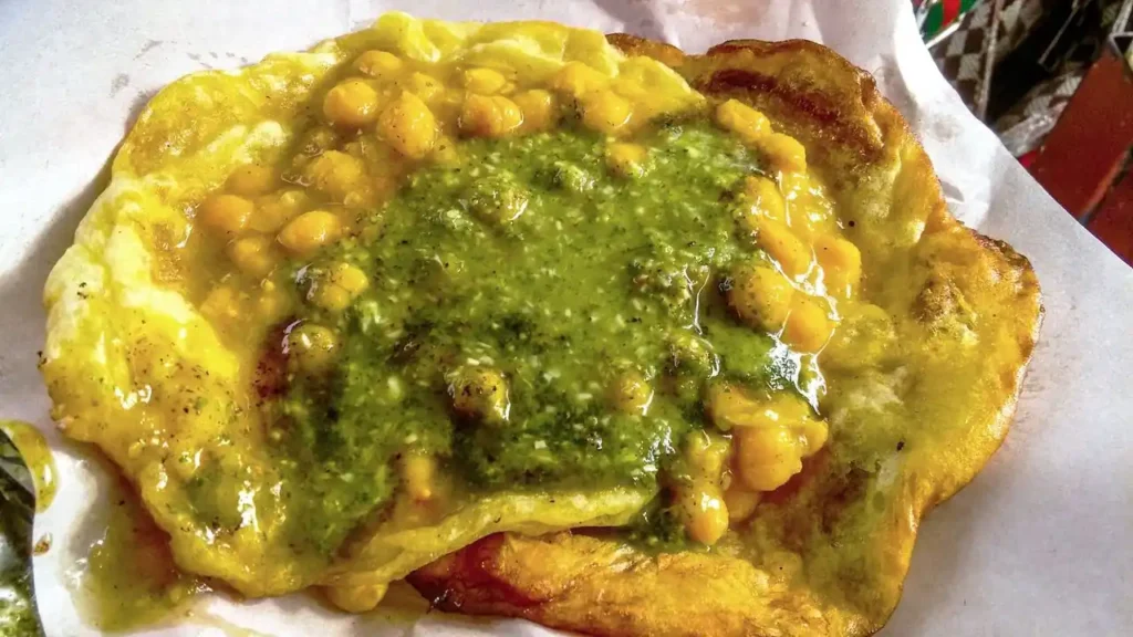 Door County vs Traverse City: Which Wins Your Heart? 17 A close-up of a Caribbean street food dish, featuring fried bread topped with curried chickpeas and bright green chutney, served on white paper.