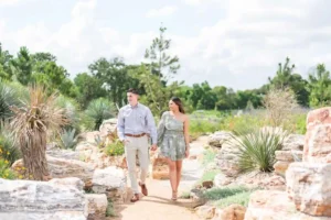 A couple walks hand in hand along a rocky garden path surrounded by greenery and desert plants under a bright, partly cloudy sky. 15 Romantic Hudson Valley Weekend for Couples Ideas